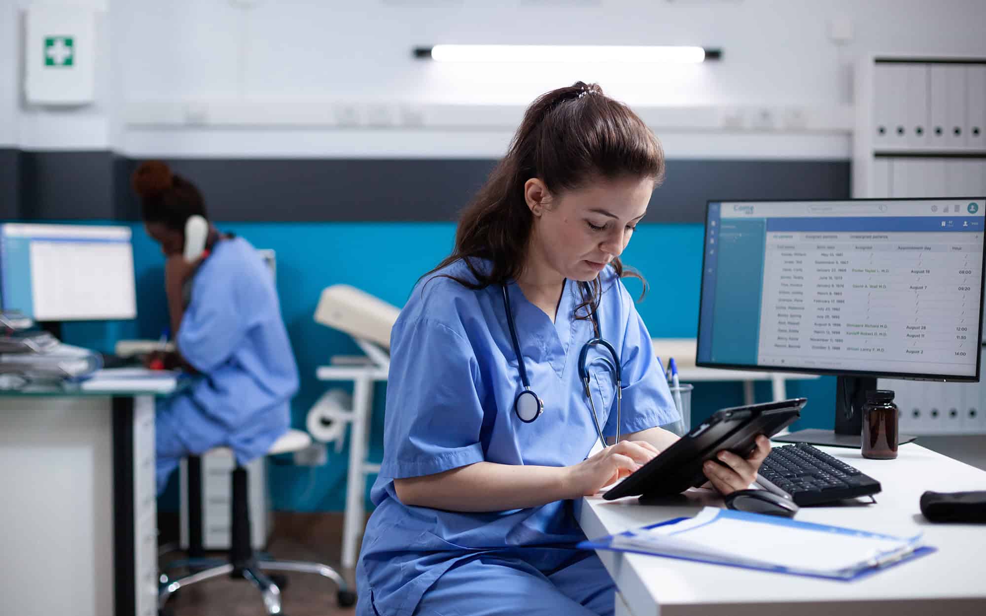 Young Nurse Checking Appointments List On Digital Tablet In Busy Medical Office